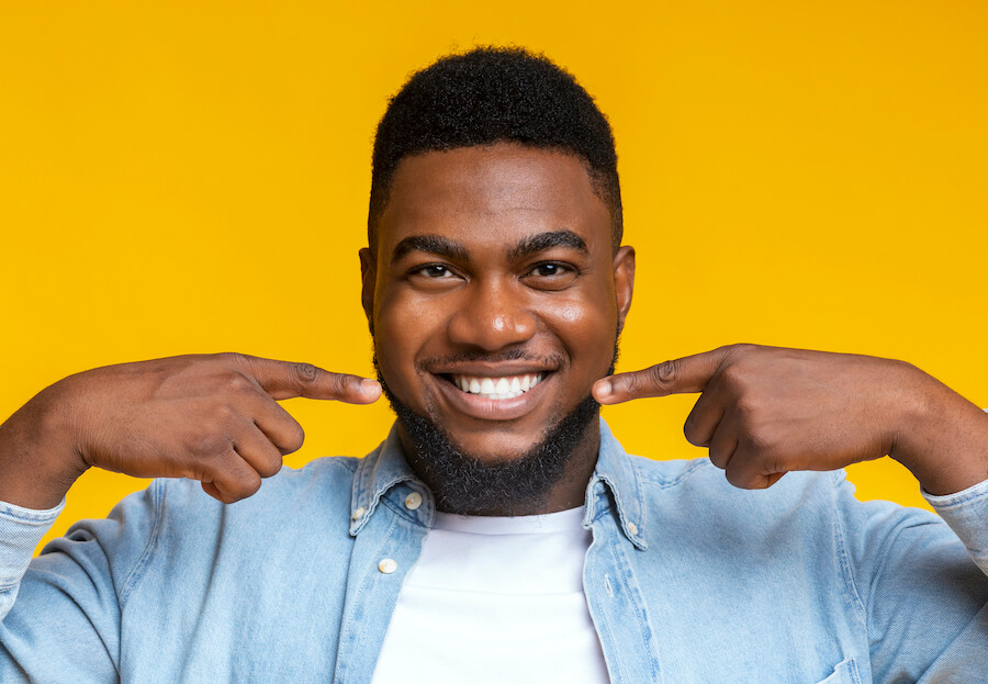 Black man smiles while pointing to his teeth against a yellow background