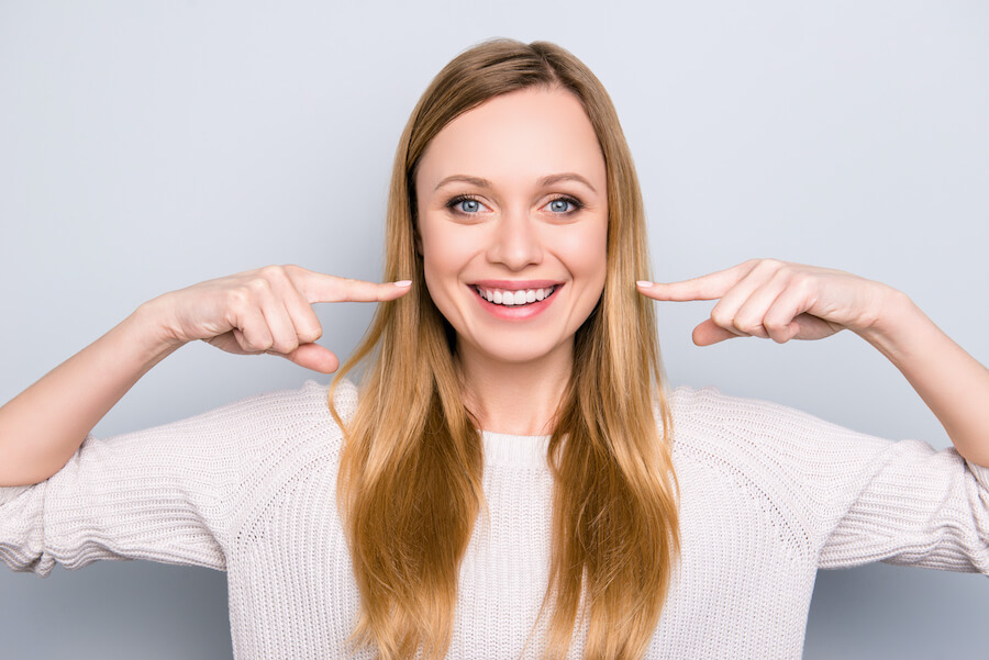 Blonde woman smiles and points to her teeth after straightening them with orthodontic treatment